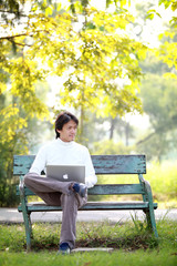 Fototapeta premium A young handsome man using laptop sitting on a bench looking in
