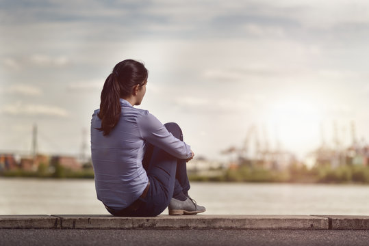 Thoughtful Woman Sits on Bench Facing at the River