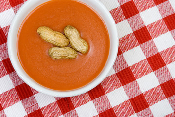 From Soup to Nuts – A bowl of tomato soup with peanuts floating in the middle. On a red checked background.