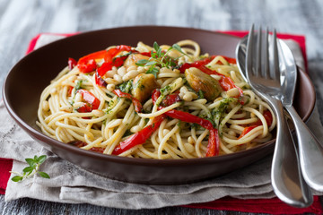 Pasta with baked sweet pepper, garlic, herb oil and pine nuts in a ceramic bowl on the wooden table