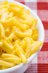 Macaroni and Cheese Meal – Macaroni pasta with cheddar cheese. In a white bowl on a red checked background.