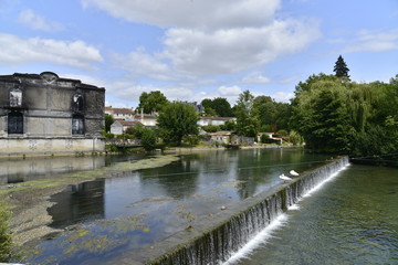 Fototapeta na wymiar Deux cygnes au bord d'une des cascades de la Charente en face du bâtiment désaffecté