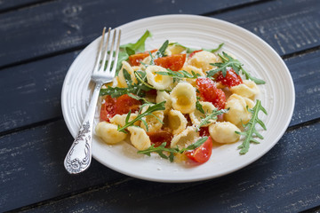 orecchiette pasta with tomatoes, Parmesan and rocket salad on a plate light on a dark wooden background