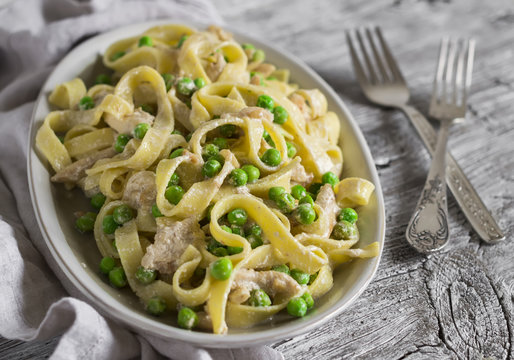 homemade pasta with green peas, chicken and cream sauce on a light wooden background