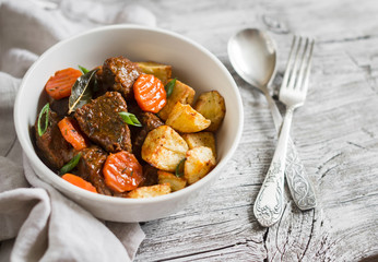 beef goulash with carrots and roasted potatoes in a white bowl on a light wooden background