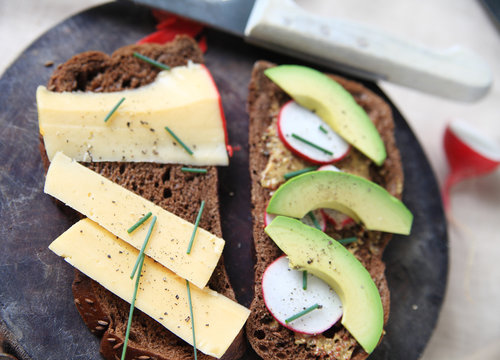 Making a sandwich on dark bread with Gouda cheese, avocado, radishes, whole-grain mustard, chives and black pepper
