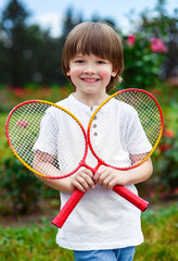 Portrait of happy little boy holding badminton rackets while