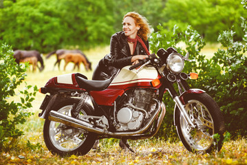 Naklejka na ściany i meble Biker girl in leather jacket on a motorcycle against the