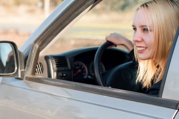 Fototapeta na wymiar Young blonde student teenage girl driving a silver car