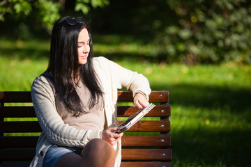 Girl with tablet sitting on a park bench