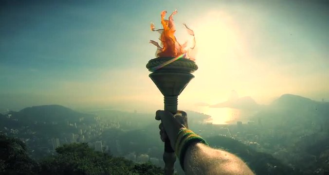 Hand of an athlete holding sport torch in silhouette against Rio de Janeiro Brazil sunrise skyline with Sugarloaf Mountain