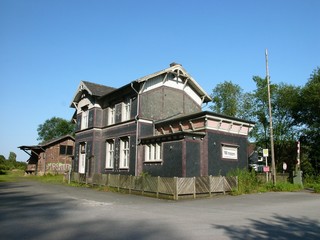 Bahnhofsgelände mit Bahnhofsgebäude und Güterschuppen vor blauem Himmel im Sonnenschein in...