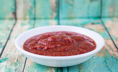 Fresh pureed tomato in white bowl over rustic wooden background