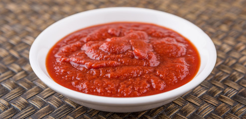 Fresh pureed tomato in white bowl over wicker background