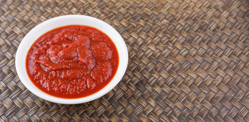 Fresh pureed tomato in white bowl over wicker background