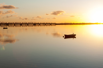 Sunrise and calmness over Tauranga Harbor. Water ripples, bird on boat and historic rail bridge on horizon.