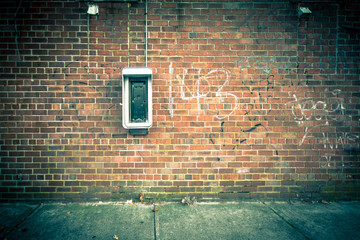 Grungy urban background of a brick wall with an old out of service payphone on it © littleny