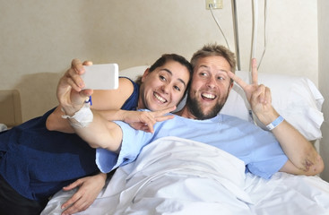 young couple taking selfie photo at hospital room with man in bed