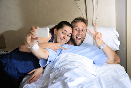 young couple taking selfie photo at hospital room with man in bed
