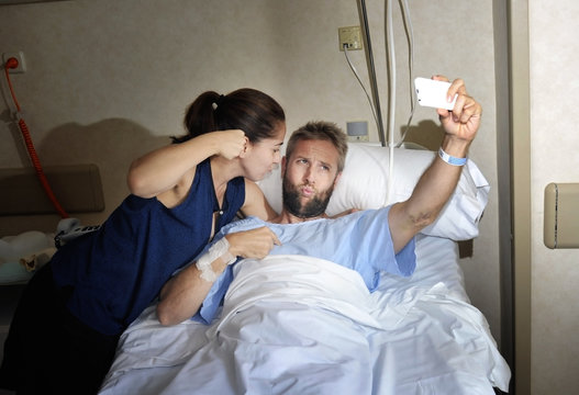 young couple taking selfie photo at hospital room with man in bed