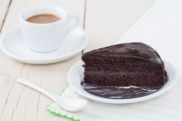 Dark chocolate cake on white plate on wooden table with coffee
