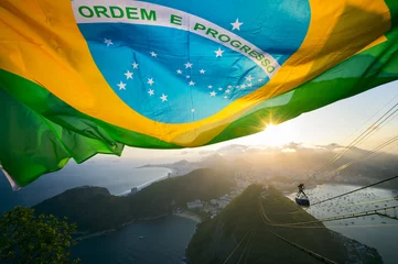 Foto auf Acrylglas Brasilien Brasilianische Flagge glänzt über der goldenen Sonnenuntergang-Stadtskyline am Zuckerhut Pao de Acucar-Berg in Rio de Janeiro Brasilien