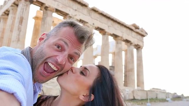 Beautiful Greek couple takes a selfie with historical Greek architecture in the background.