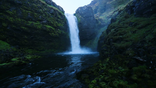 Powerful Waterfall plunging into a blue pond in a green mountain valley. Close approach by drone.