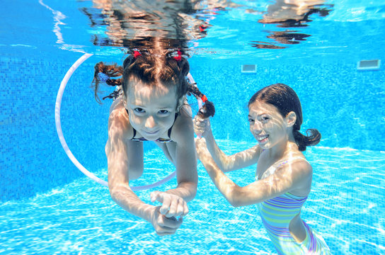 Happy children swim in pool underwater, girls swimming, playing and having fun