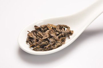 Heap of dry green tea leaves in white ceramic spoon
