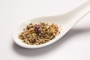 Heap of dry medical herbal tea in white ceramic spoon