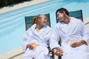 beautiful young couple resting in deck chairs with bathrobe by the pool of a thalasso resort - obrazy, fototapety, plakaty