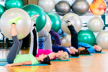 Young and senior people exercising with ball in gym