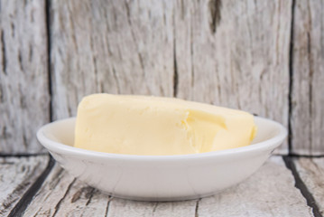 A block of butter in white bowl over rustic wooden background