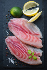 Close-up of raw tilapia with seasonings on a stone slate dish