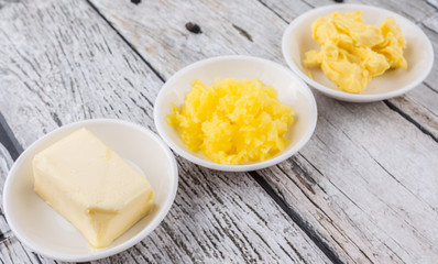A block of butter, margarine and ghee in white bowls over rustic wooden background