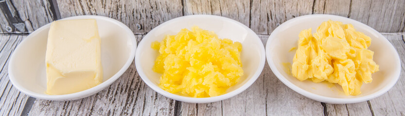 A block of butter, margarine and ghee in white bowls over rustic wooden background