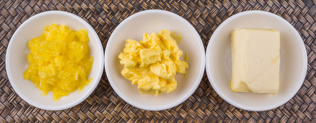 A block of butter, margarine and ghee in white bowls over wicker background