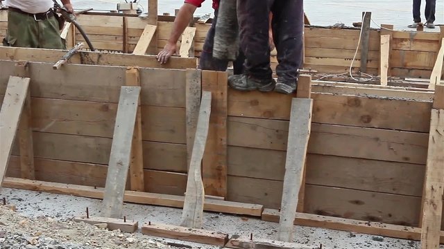 Concrete is being poured with continuous casting. Workers are pouring cement in the wooden formwork at construction site.
