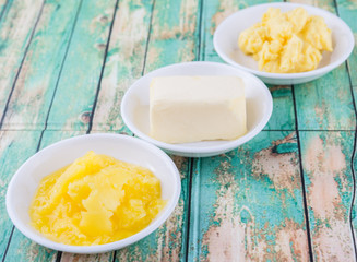 A block of butter, margarine and ghee in white bowls over rustic wooden background