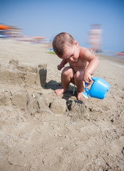 Little boy playing with sand and watering can at sea italy beach