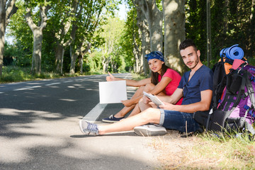 cheerful young couple backpacker hitchhiking on a roadside in summer vacation