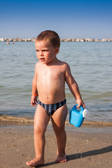 Little boy playing with sand and watering can at sea italy beach