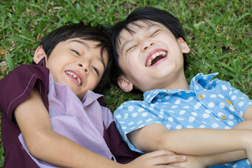 Two Little boy lay down on green grass and laugh
