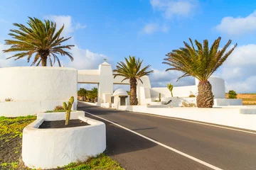 Poster Road with palm trees and white entry gate to Costa Teguise town, Lanzarote, Canary Islands, Spain © pkazmierczak