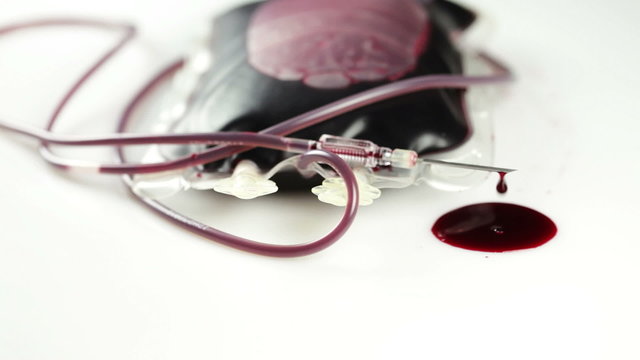A leaking blood donation bag, needle and drops of blood