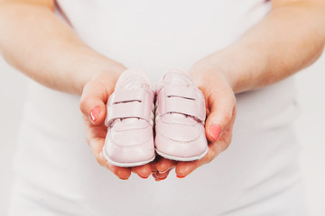Pregnant woman belly holding pink baby booties, expecting girl - Powered by Adobe