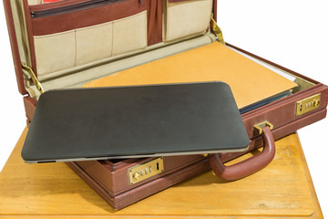 black laptop and brown envelope in openned old vintage brown briefcase on wood table isolated