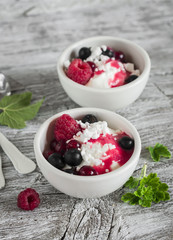 cottage cheese with berries and berry puree in a white bowl on a light wooden background