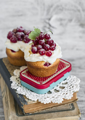 cupcakes with cream and red currants on a light wooden background, vintage style